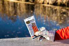 Load image into Gallery viewer, Hot & spicy munchies held by gloved hand by water.